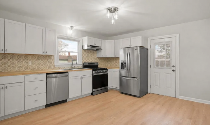 After shot of a kitchen with white cabinets, wood floors and countertops, and stainless steel appliances, taken from a successful Borrower rehab project funded by Marie William Capital.